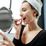 A woman checks her clear aligners in a handheld mirror